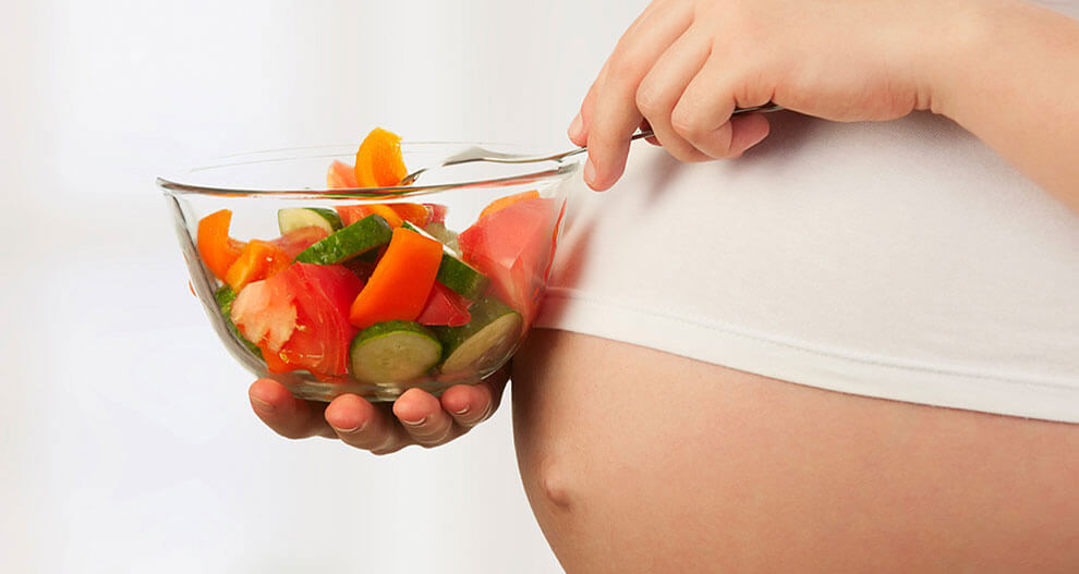 A pregnant woman holding a bowl of fresh vegetables.