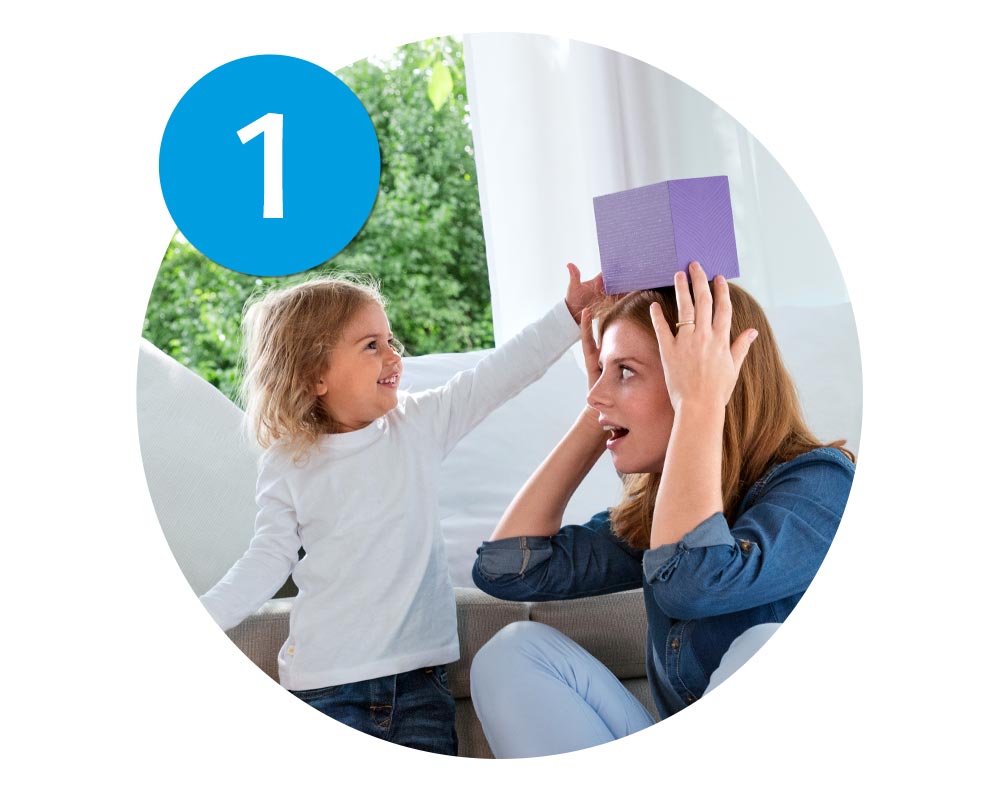 A child places a purple box on a woman's head.