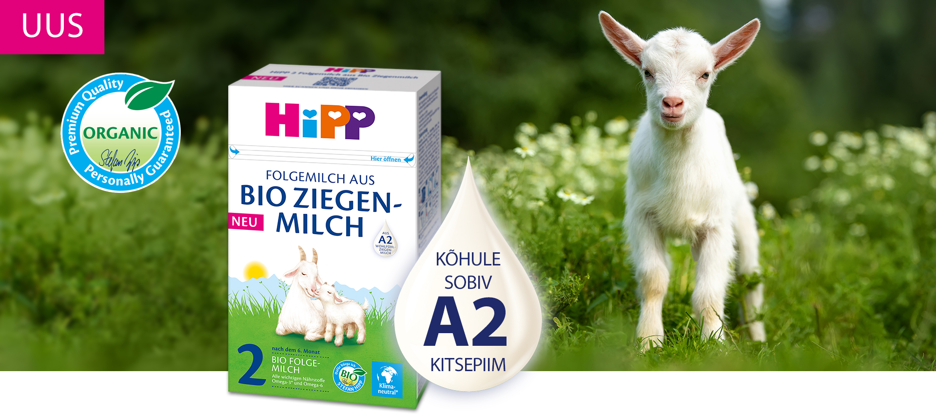 Valge kits seisab rohelisel, valgete lilledega niidul, Hippi beebitoidukarbi kõrval, millel on kitse illustratsioon ja sõna "orgaaniline".
