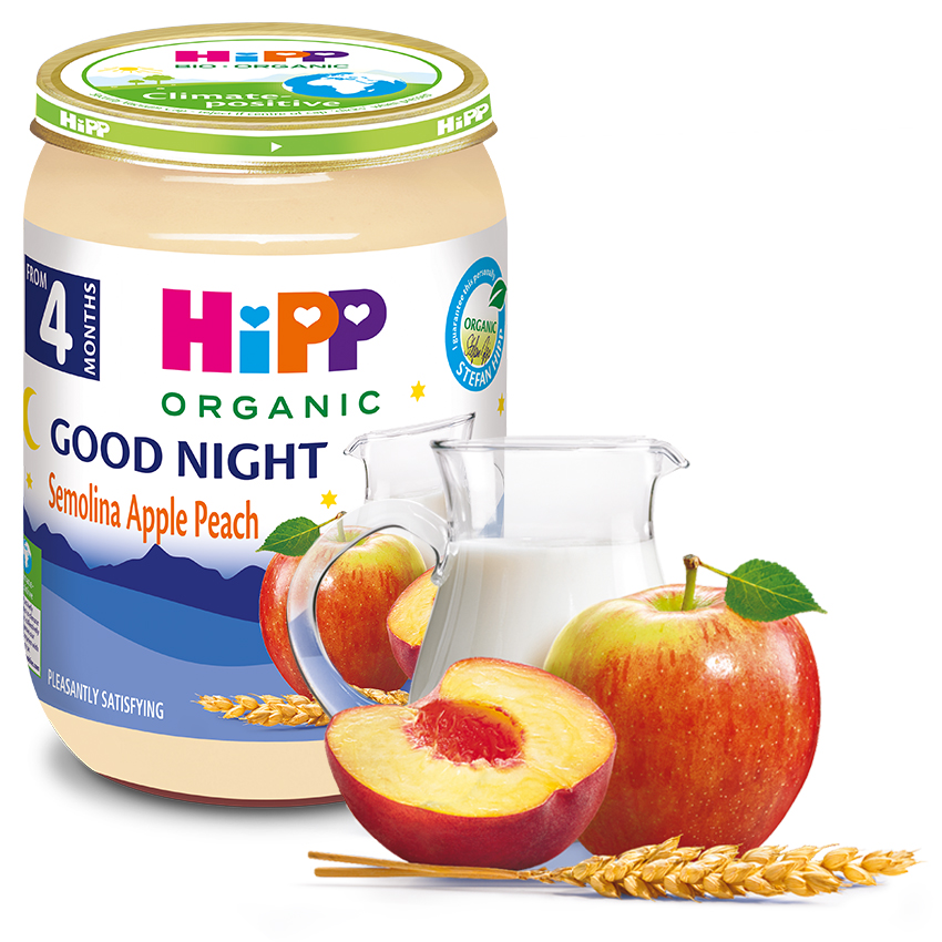 Mahepõllumajandusliku imikutoidu purk sildiga "Good Night Semolina Apple Peach" on välja pandud kõrvuti klaaskannuga, mis on täidetud piima, terve õuna, viilutatud õuna ja nisukõrvaga.