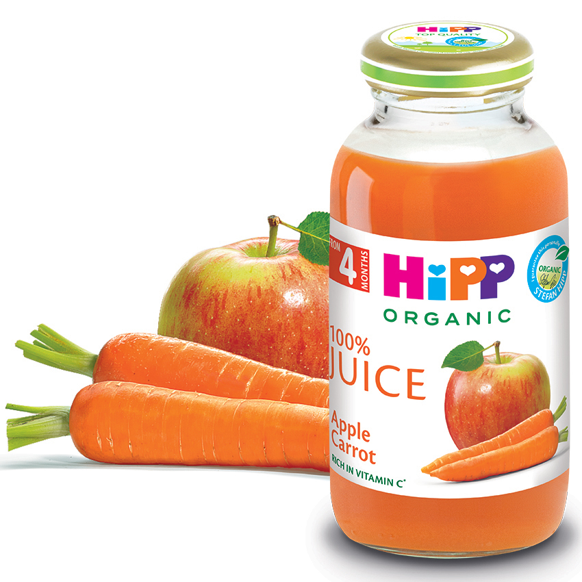 Läbipaistev klaaspudel, mis on täidetud apelsinimahlaga, millel on märge "100% Juice Apple Carrot" ja "Organic", ning mille kõrval on värske õun ja kolm porgandit.